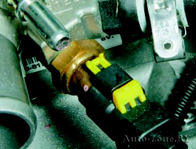 Отсоедините колодку жгута проводов от датчика температуры охлаждающей жидкости, сдвинув замок фиксатора (желтого цвета) колодки и нажав на фиксатор