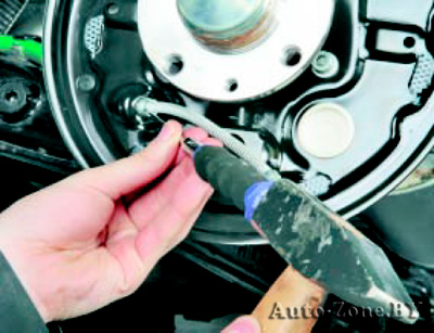 Выпрессуйте наконечник троса стояночного тормоза из отверстия в щите тормозного механизма заднего колеса